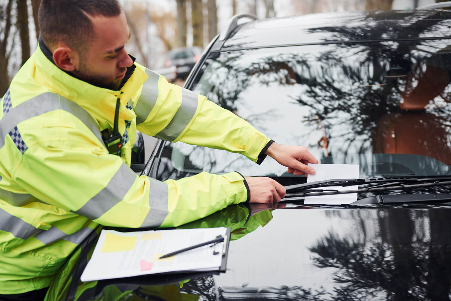 Male parking officer placing parking ticket under windscreen wiper of parked car.